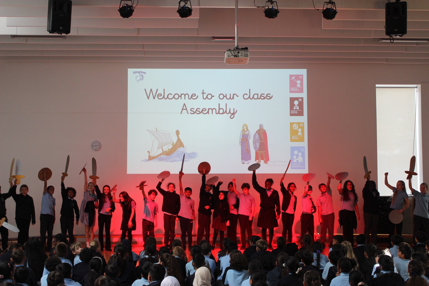 Class 6L at the front of the hall holding up cardboard swords and shields
